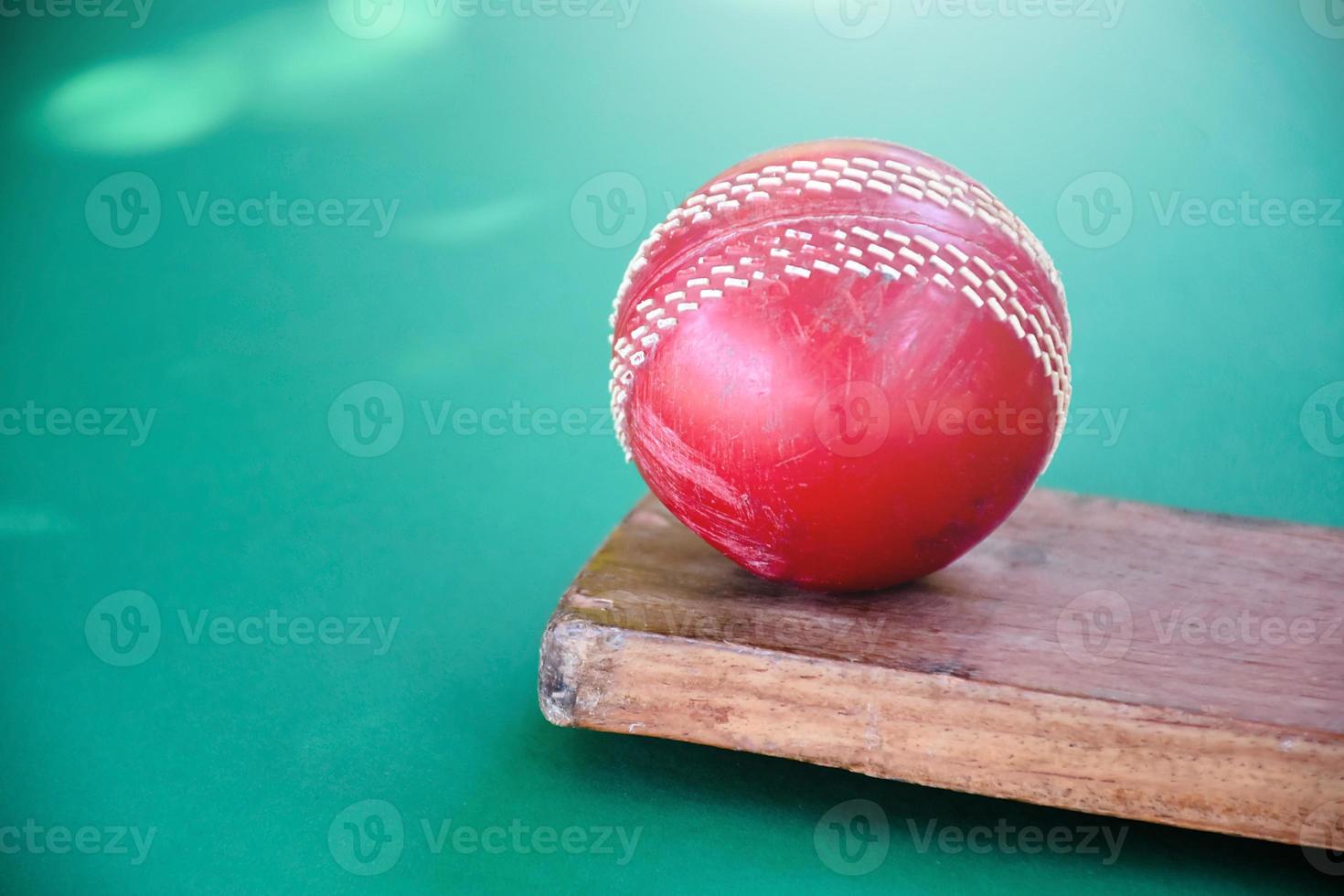 Closeup old cricket sport equipments on green floor, old leather ball, wooden bat, soft and selective focus, traditional cricket sport lovers around the world concept. photo