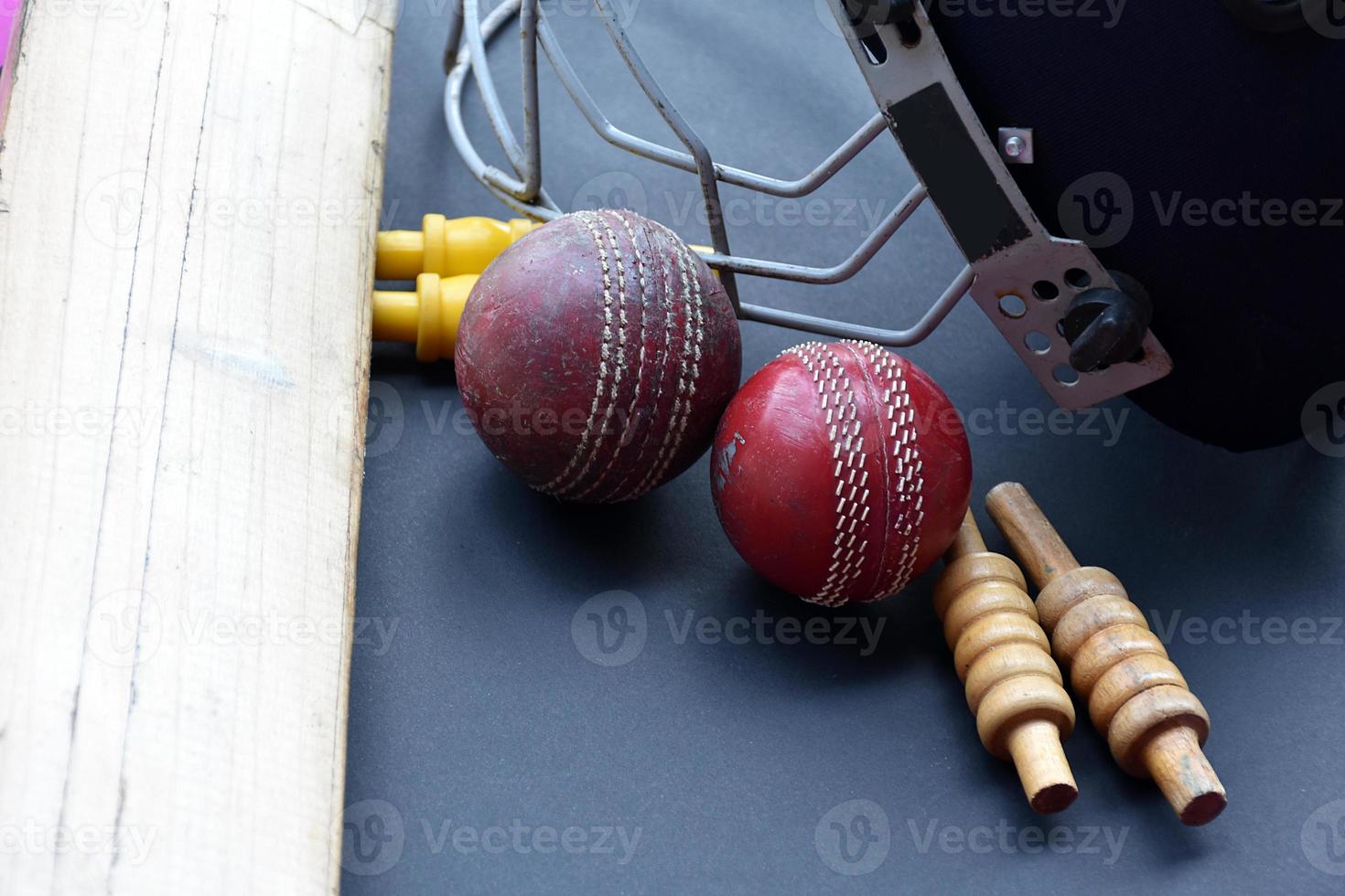 Old training cricket sport equipments on dark floor, leather ball, wickets, helmet and wooden bat, soft and selective focus, traditional cricket sport lovers around the world concept. photo