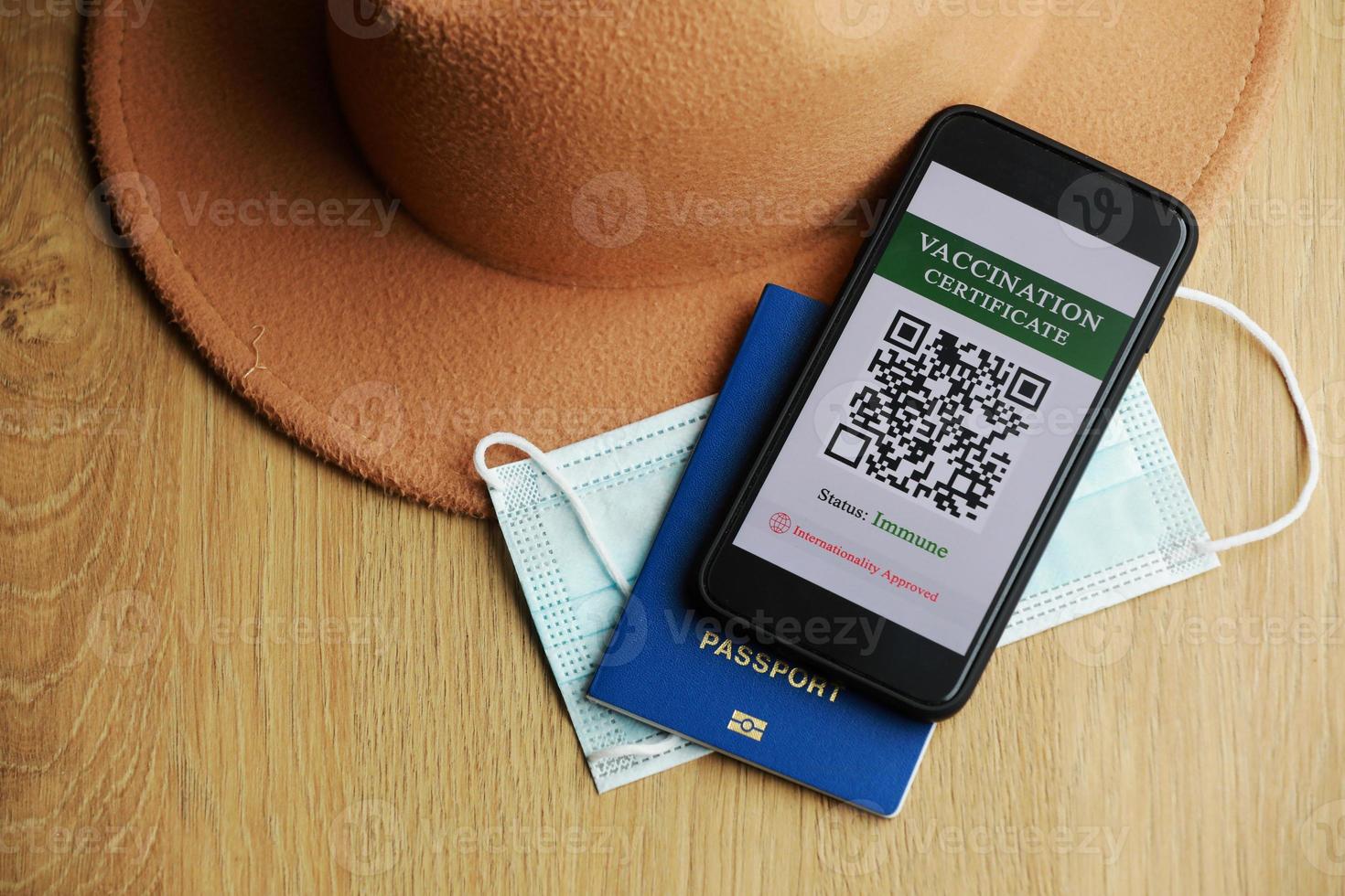 New normal concept. Close up view of a smartphone with an immune digital health passport. In the wooden background, protective mask, hat and passport. photo