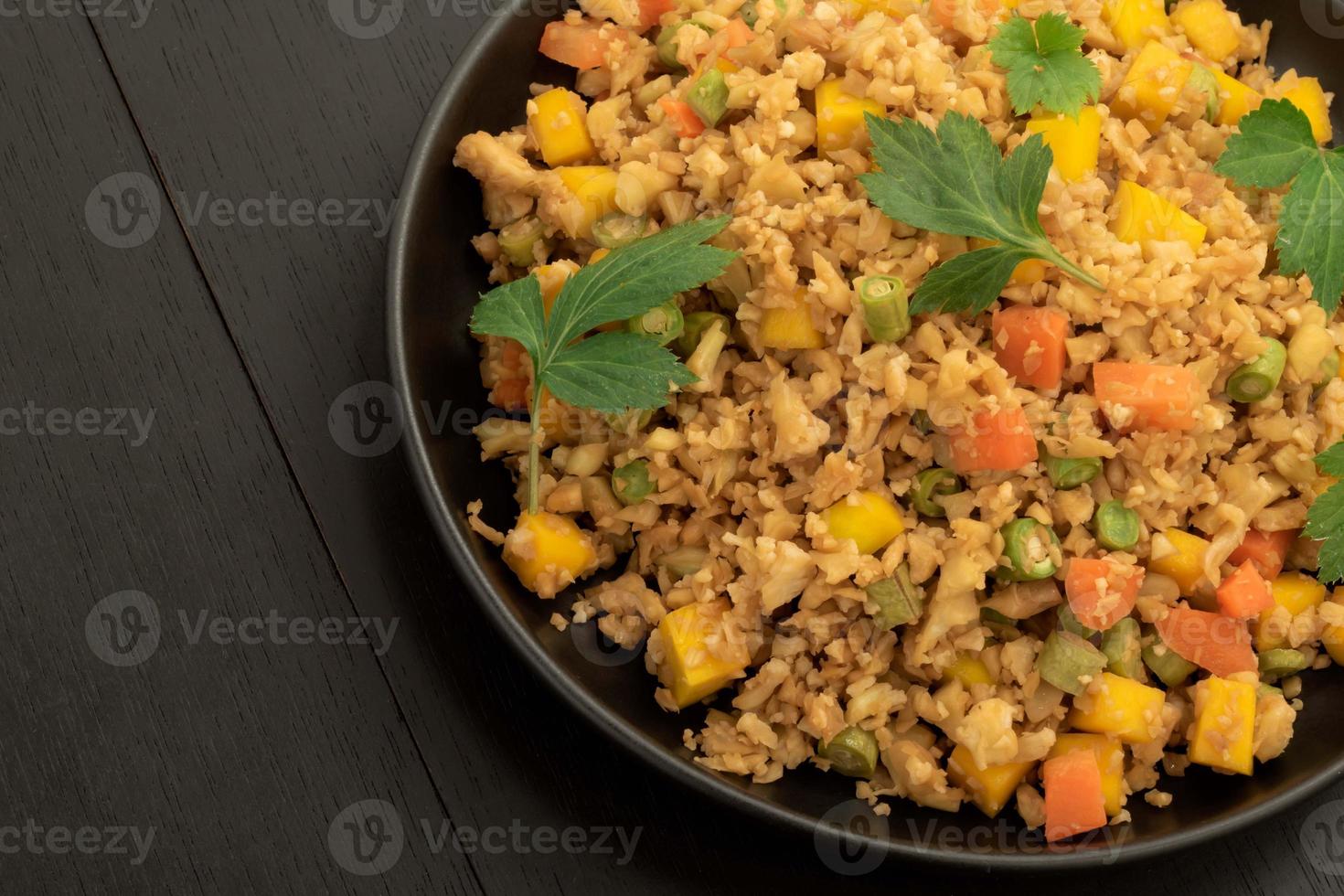 el arroz frito con coliflor tiene vegetales en un plato negro sobre una mesa de madera. foto