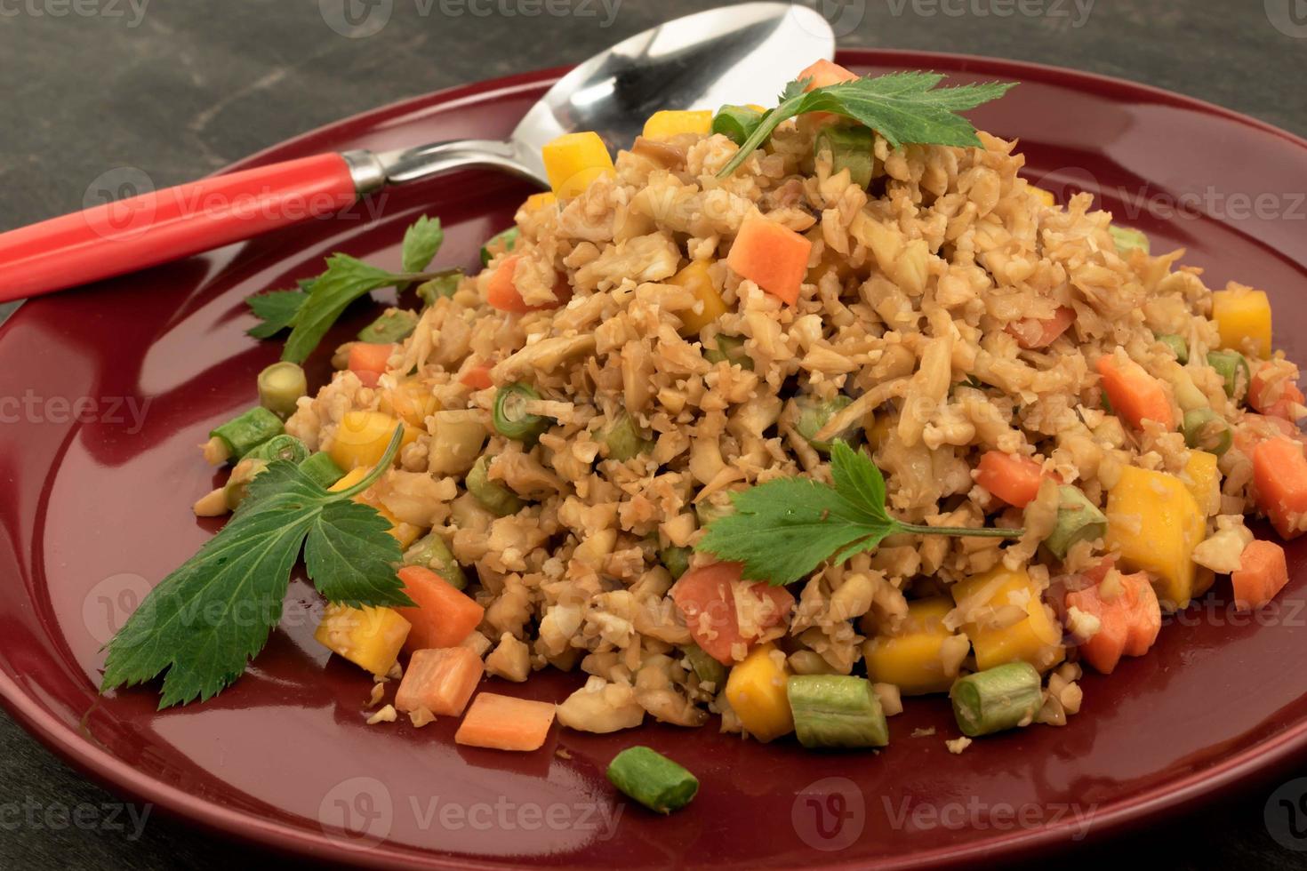 el arroz frito con coliflor tiene vegetales en un plato rojo sobre una mesa de madera. foto