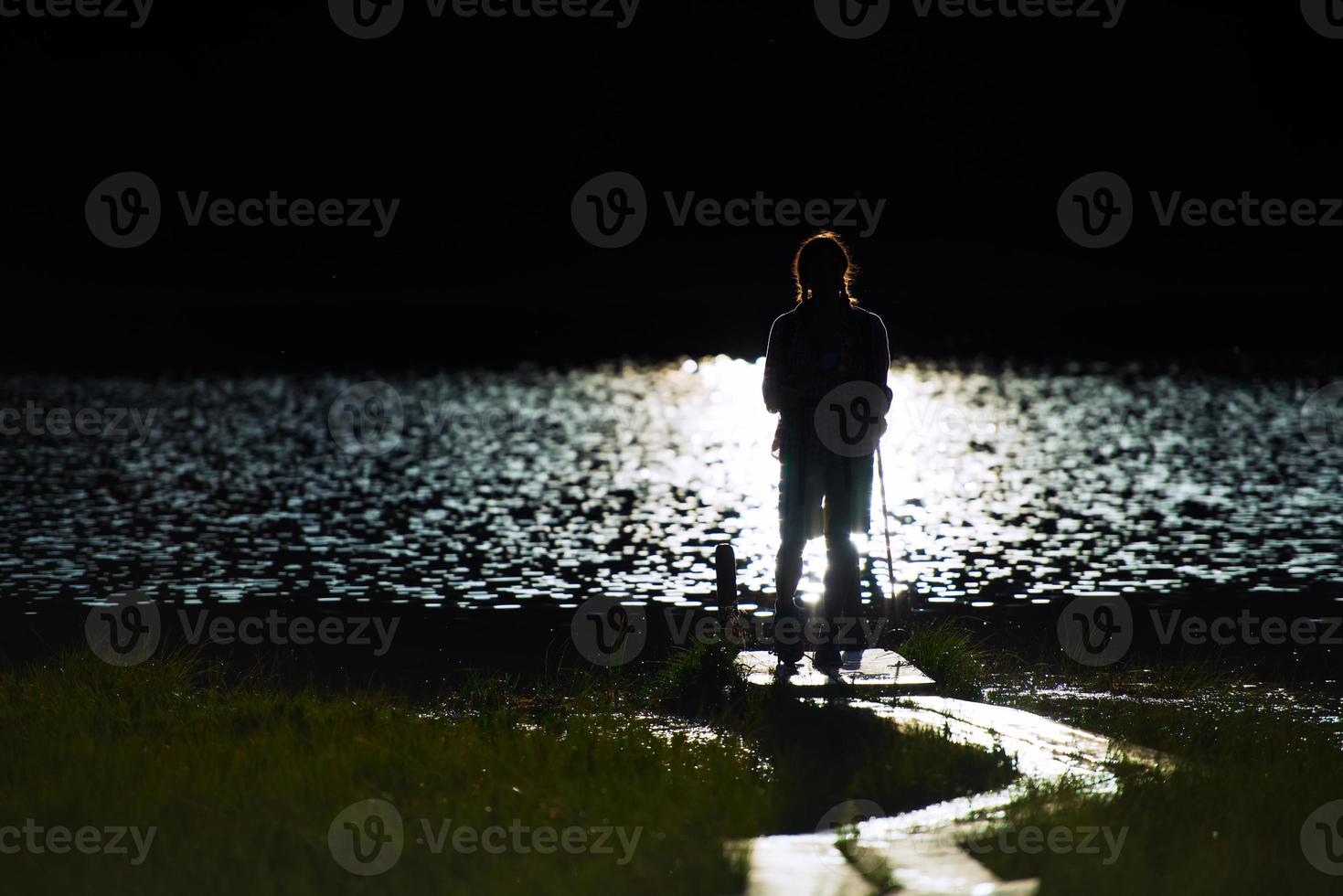 Young girl in hike in  silhouette on the small pier of a mountain lake photo