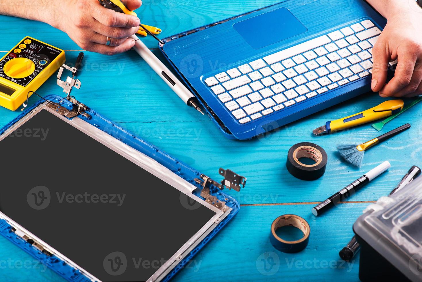 el asistente repara la computadora portátil con herramientas y manos en la mesa de madera azul. vista superior foto