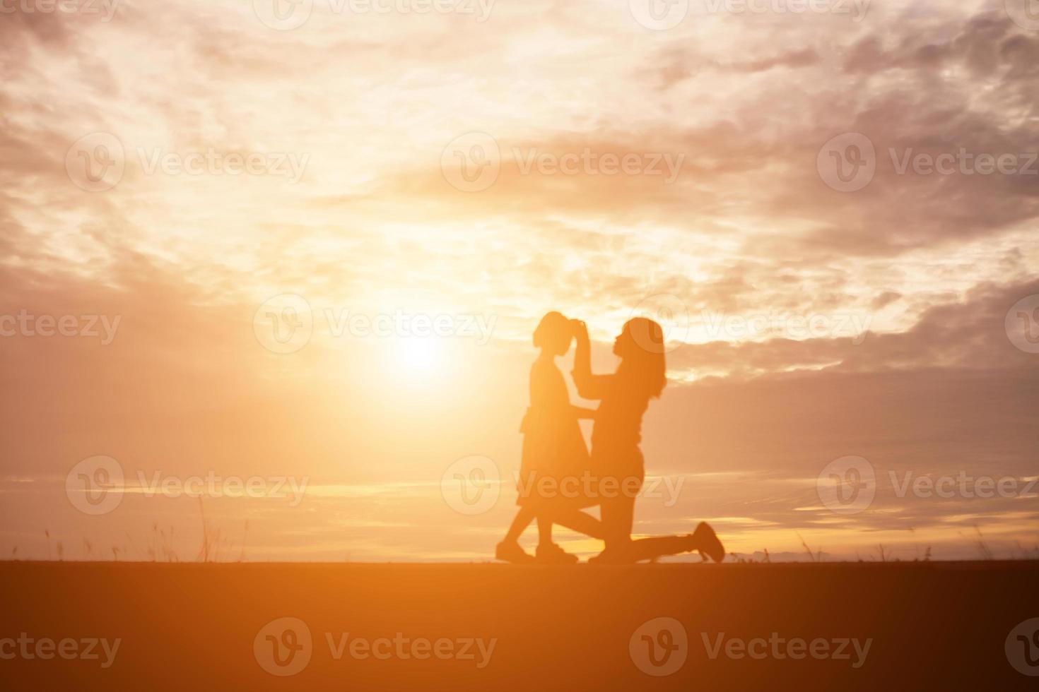 una silueta de una niña feliz los brazos de su madre amorosa para un abrazo, frente a la puesta de sol en el cielo en un día de verano. foto