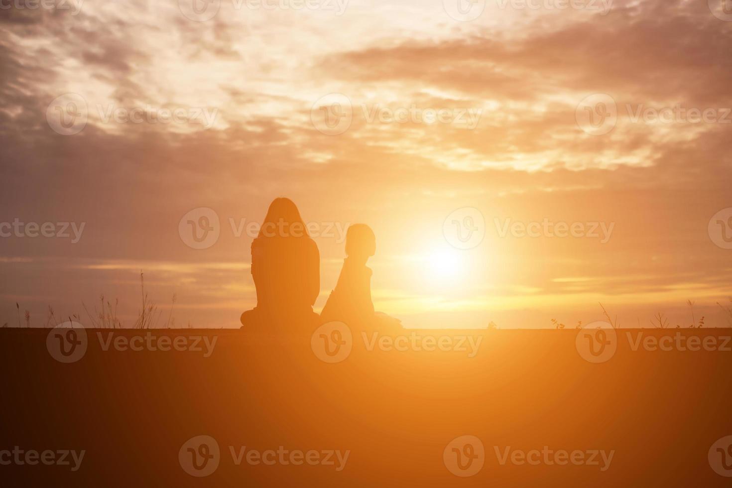 a silhouette of a happy young girl child the arms of his loving mother for a hug, in front of the sunset in the sky on a summer day. photo