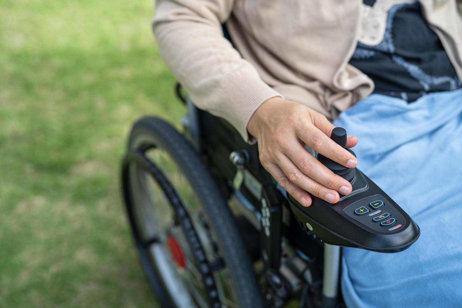mujer asiática paciente en silla de ruedas eléctrica con joystick y control remoto en la sala del hospital de enfermería, concepto médico fuerte y saludable foto