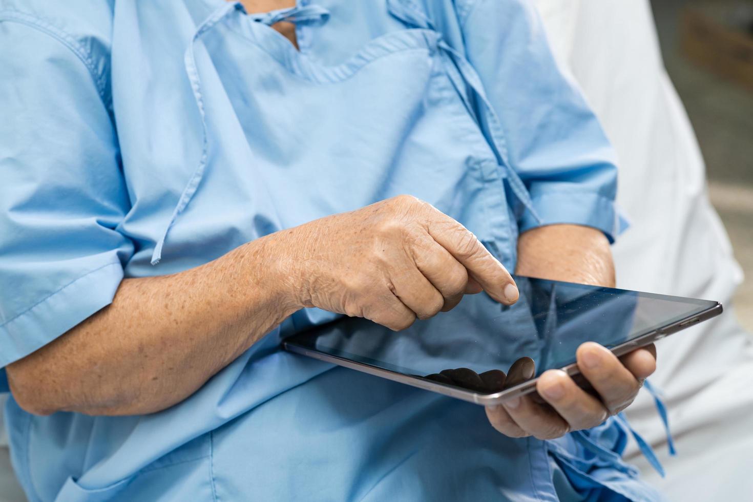 Asian senior or elderly old lady woman patient holding in her hands digital tablet and reading emails while sitting on bed in nursing hospital ward, healthy strong medical concept photo