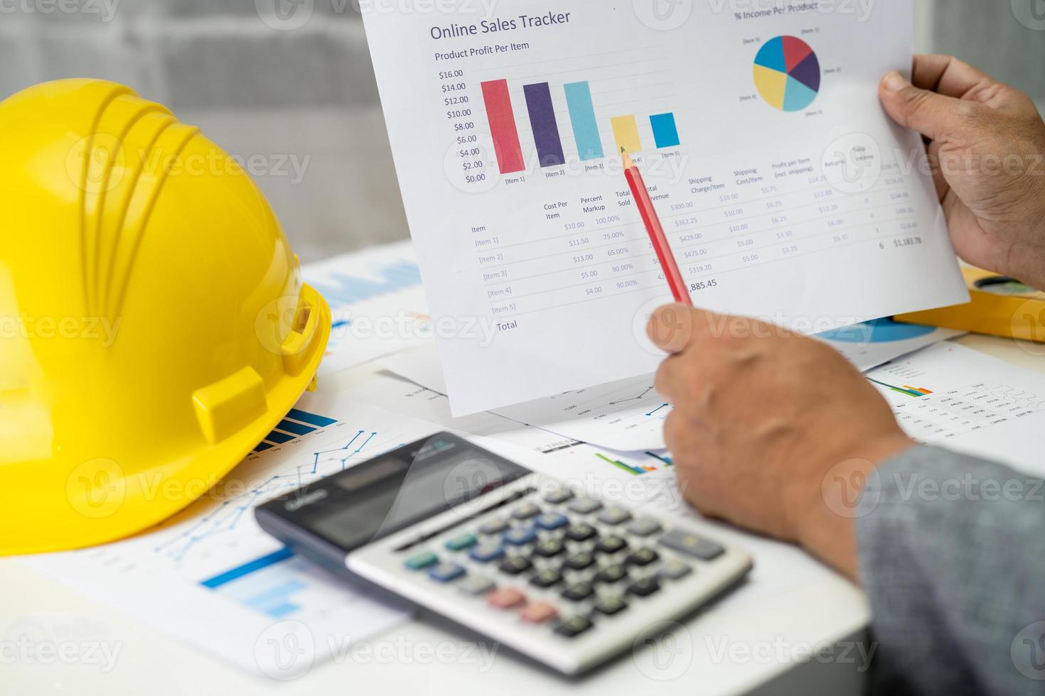 Asian engineer with architectural house plan project blueprint, graph and yellow helmet and engineering construction tools. photo
