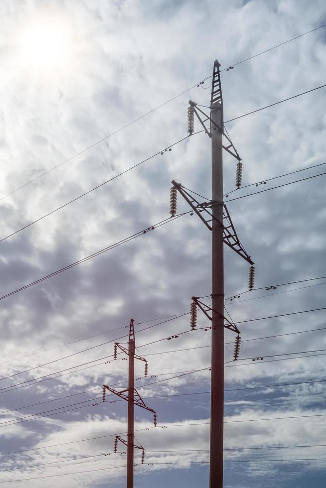 Two high-voltage towers with a concrete base against a cloudy sky. photo
