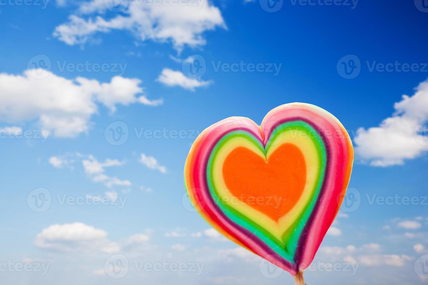 Colorful heart shaped lollipop on sky background photo