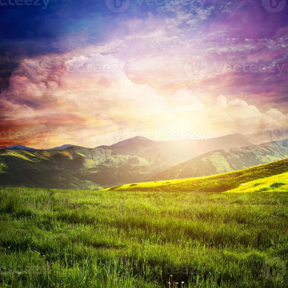 Fairtytale landscape with green grass, mountains, sunset fantastic sky. photo