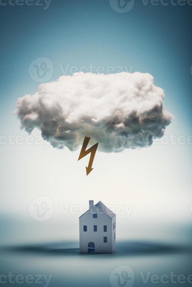 Paper house standing under a white cloud with yellow lightning photo