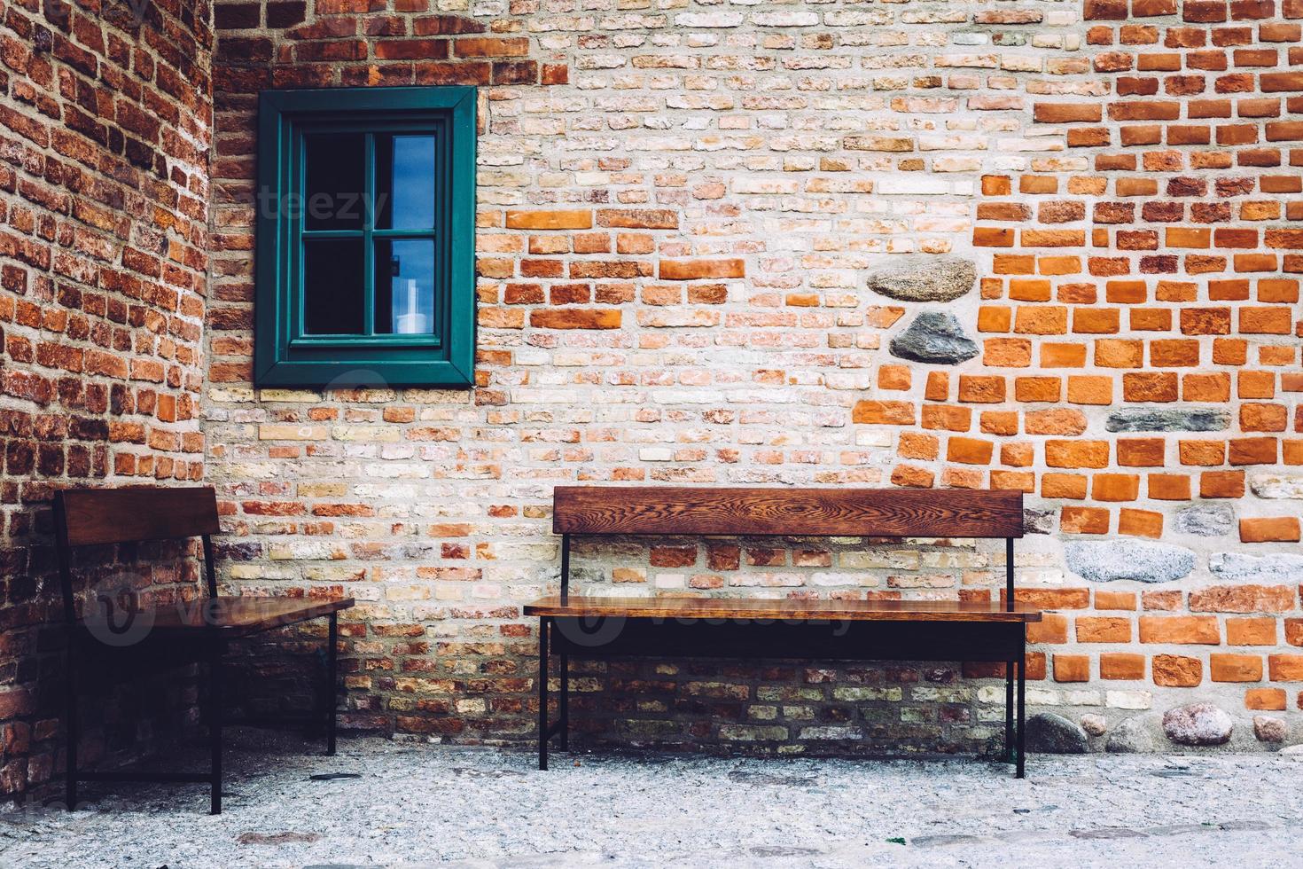 Two benches standing in front of old building with green window. photo