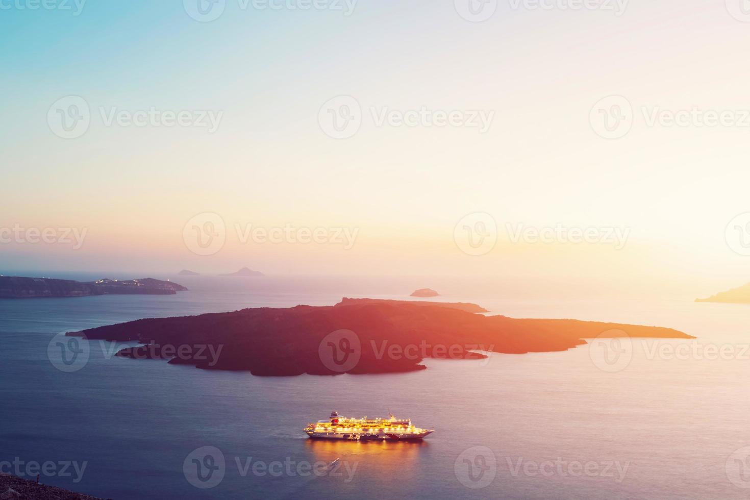 Tourist ship cruiser sailing next to Nea Kameni. Santorini, Greece at sunset photo