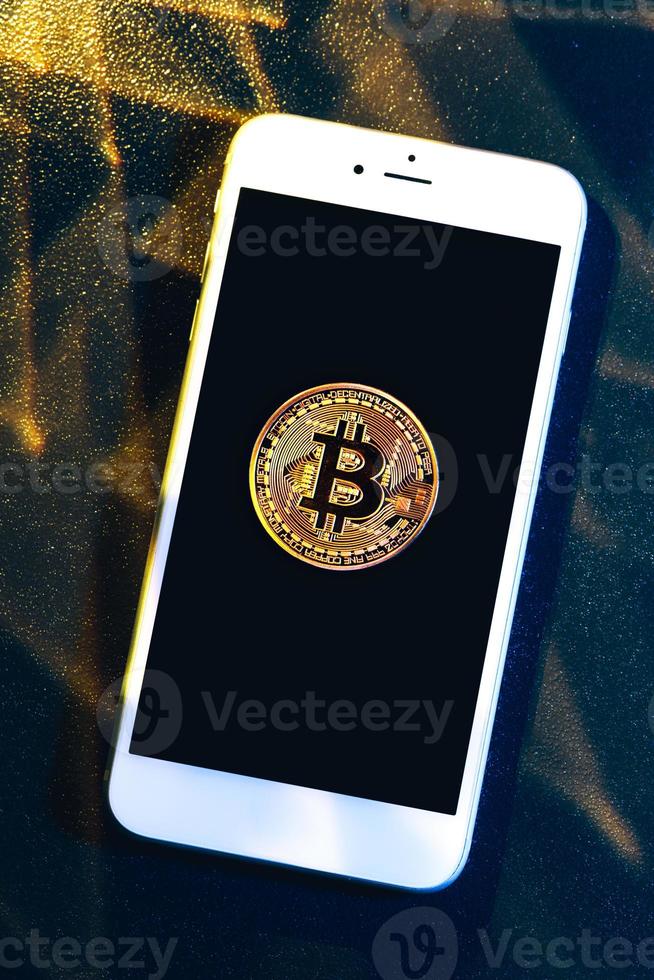 Phone with a bitcoin laying on top of it. photo