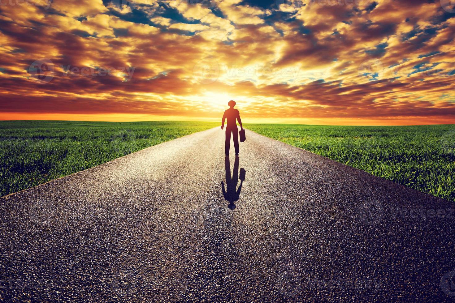 Man with suitcase and hat on long straight road towards sunset sky photo