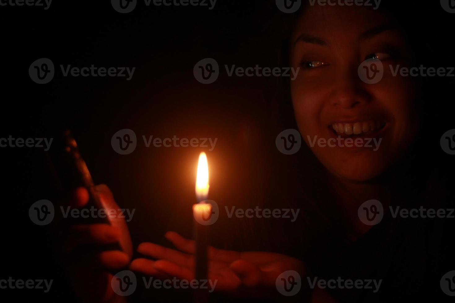 mujer asiática sonriendo a su celular con velas en la noche oscura foto