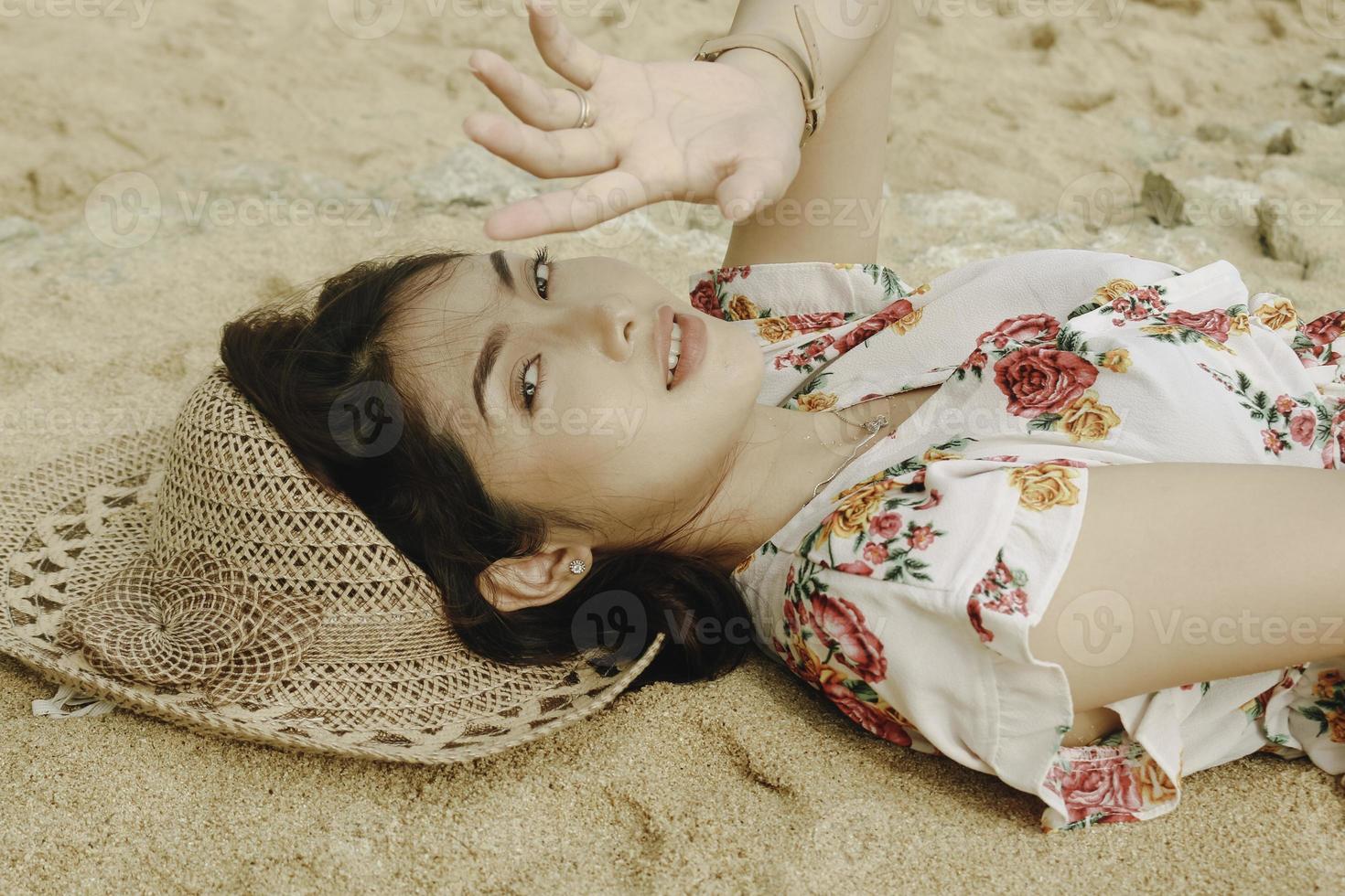 A young beautiful Asian woman dazzled by the light while lying on the beach sand photo