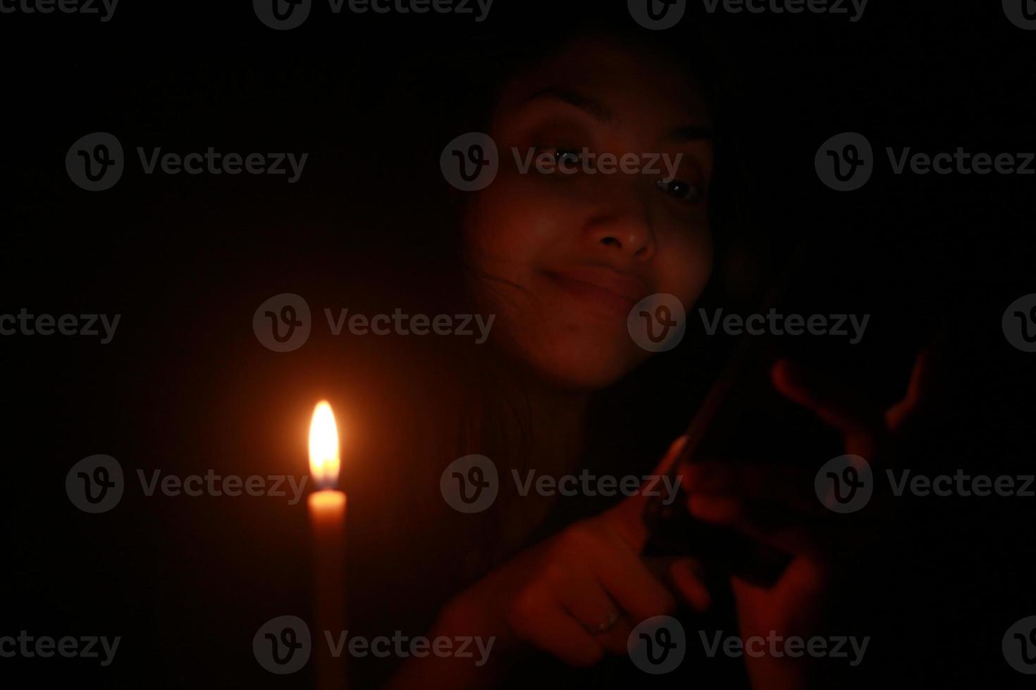 Asian woman smiling to her cellphone with candle in the dark night photo