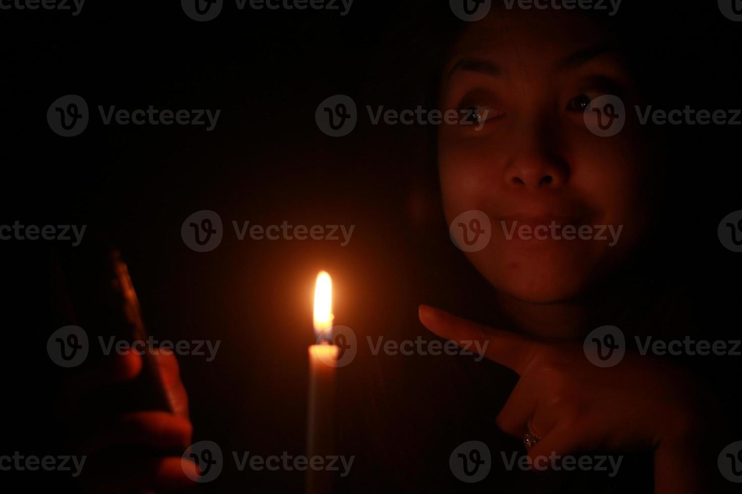 Asian woman smiling to her cellphone with candle in the dark night photo