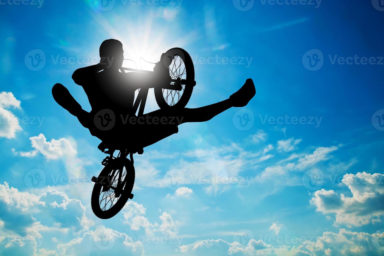 Man jumping on bmx bike performing a trick against sunny sky photo