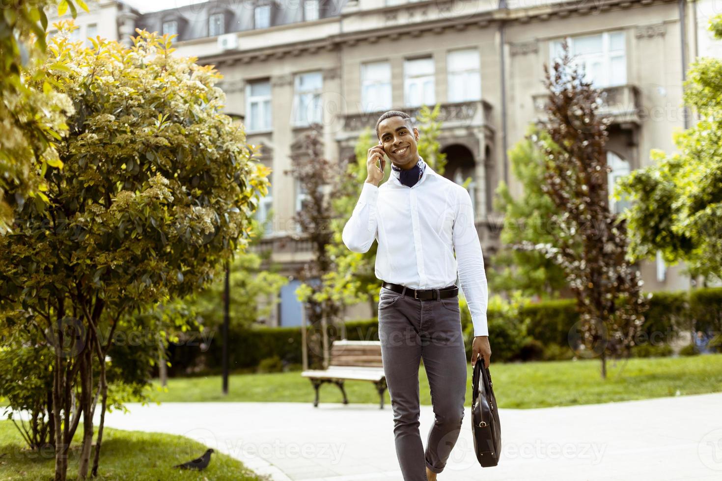 Young African American businessman using a mobile phone while walking on a a street photo