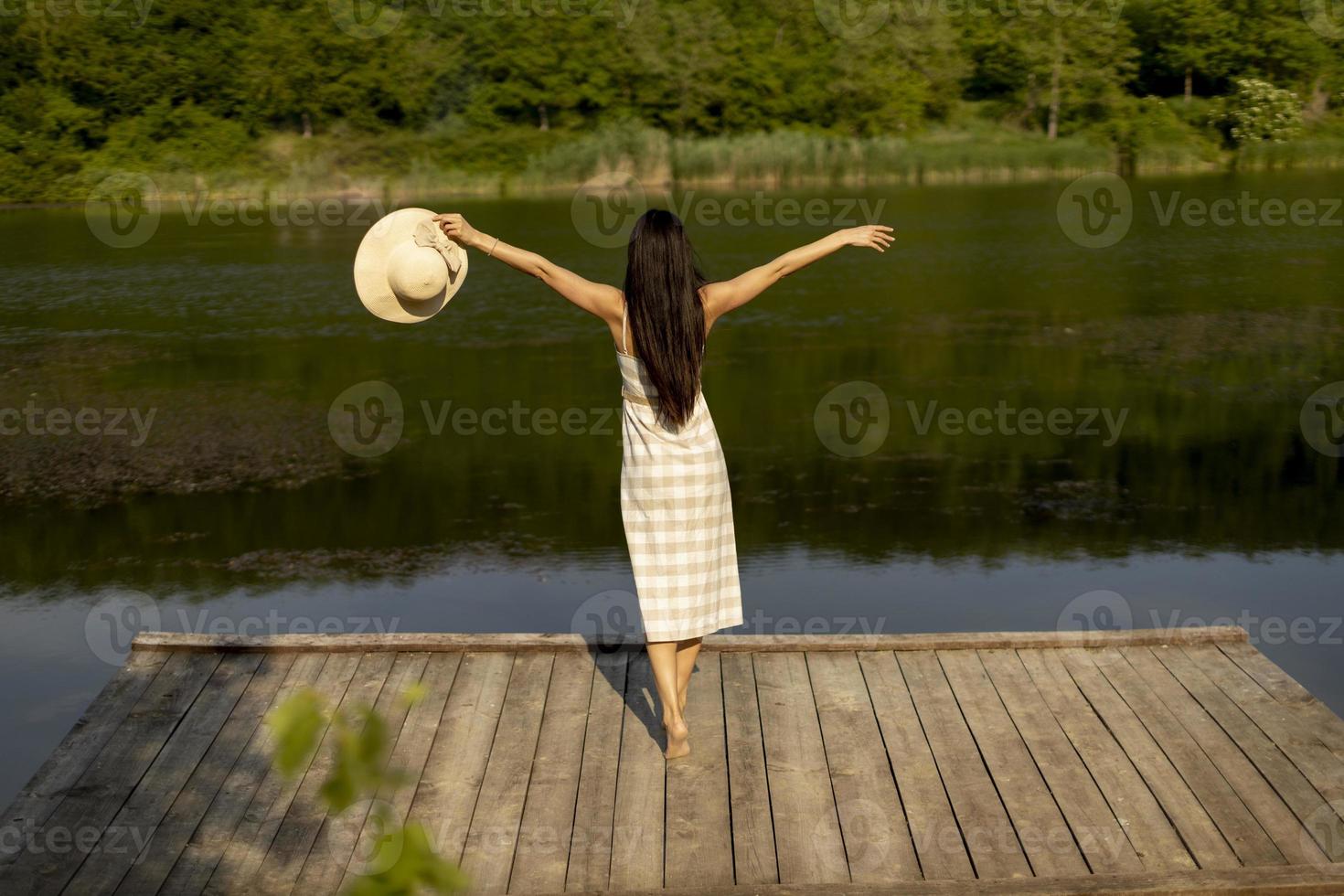 Young woman standing on the wooden pier at the calm lake photo