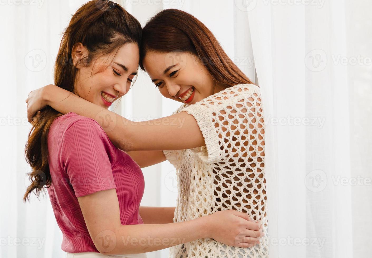 Romantic gay lesbians holding each other smiling. Beautiful sensual Asian homosexual couple intimate moment embracing in bedroom by window. Portrait of two women hugging with affectionate relationship photo