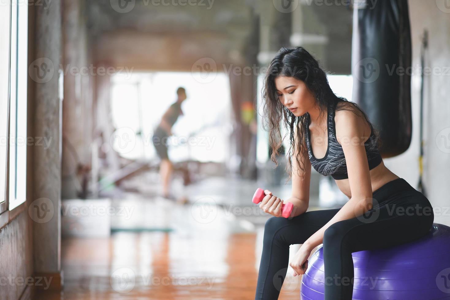 mujer deportiva en forma asiática sentada en la pelota y haciendo ejercicio con pesas en la sala de pesas en el gimnasio. concepto de fitness de mujer deportiva foto