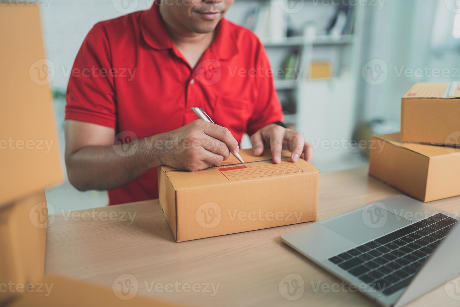 Asian delivery man worker in red uniform work at home , checking list parcel boxes for sending or conveying parcels by mail. photo