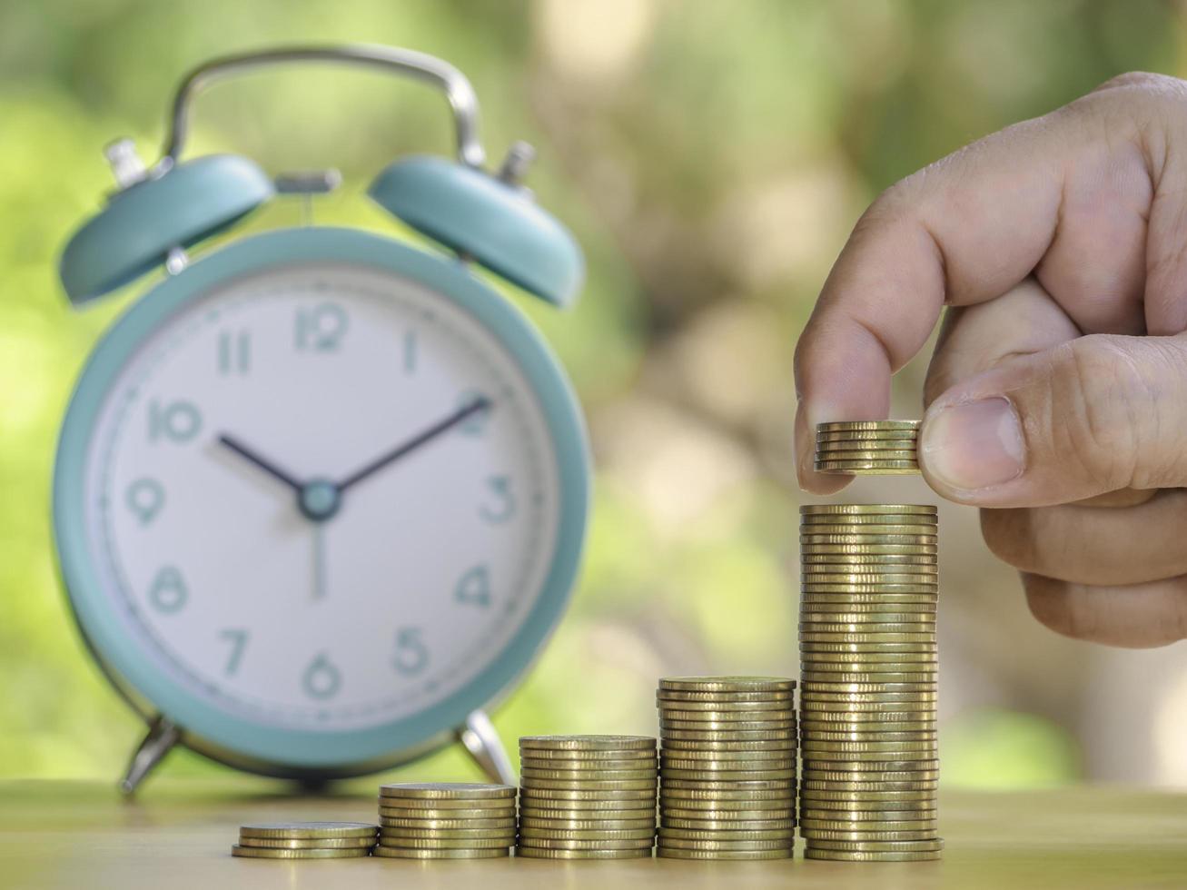 Hand are stacking coins with alarm clock to save the financial stability for the future. Concept for loan, property ladder, financial, mortgage, real estate investment, taxes and bonus. photo