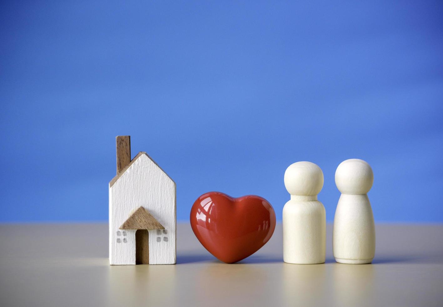 figura familiar de madera parada cerca del corazón rojo y el símbolo de la casa en miniatura. concepto de amor por la relación familiar, vida de pareja y felicidad con antecedentes azules. foto