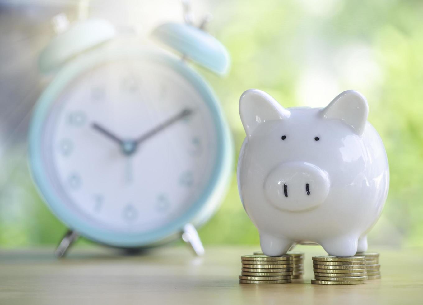 White piggy bank on gold coins stack 4 rows with alarm clock placed on wooden table to save money invest for future.Concept for loan, property ladder, financial,real estate investment, tax and bonus. photo