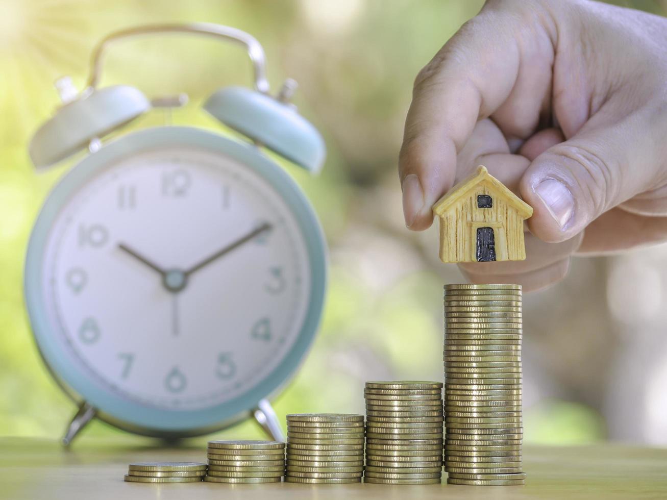 Hand are stacking coins and home with alarm clock to save the financial stability for the future. Concept for loan, property ladder, financial, mortgage, real estate investment, taxes and bonus. photo