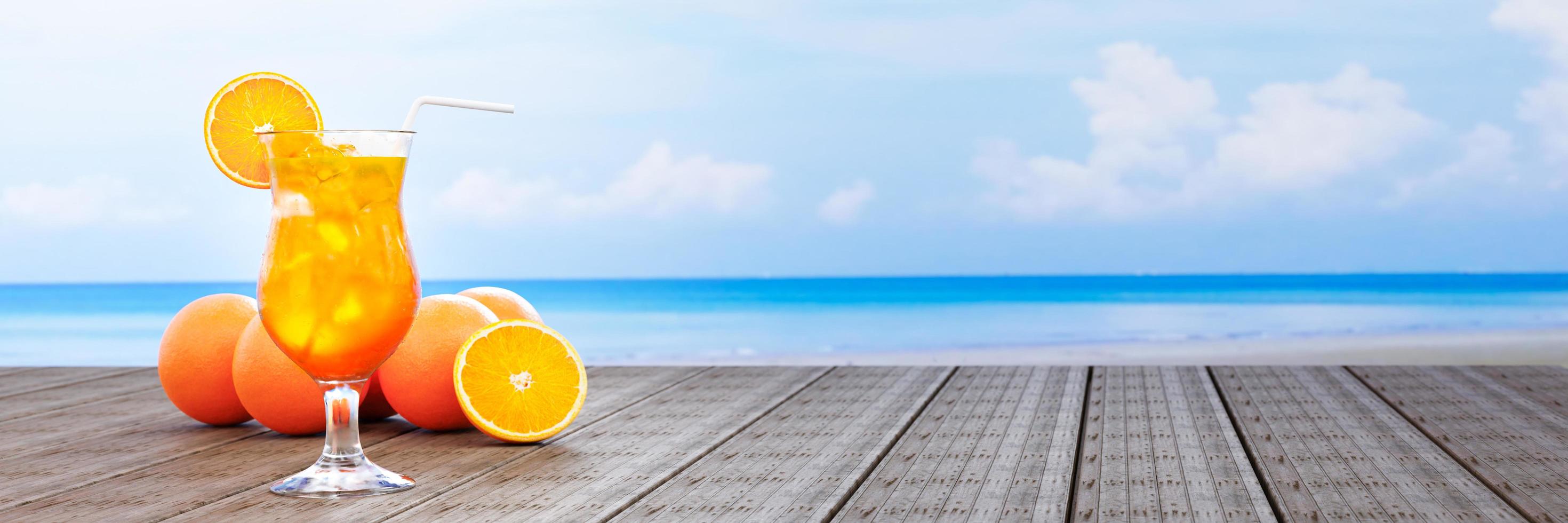 jugo de naranja en un vaso transparente con cubitos de hielo y jugo de naranja en la boca del vaso. bebidas frías colocadas en el balcón de madera junto al mar en medio del día. representación 3d foto