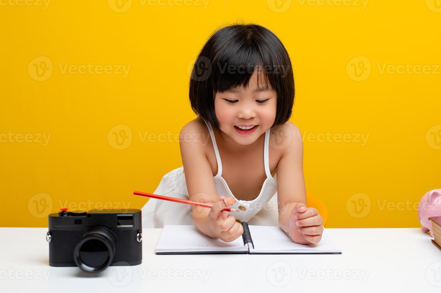 cute girl pictures Asia writes a book In the office for hardworking kids. Smart kids. White table on a yellow background. photo