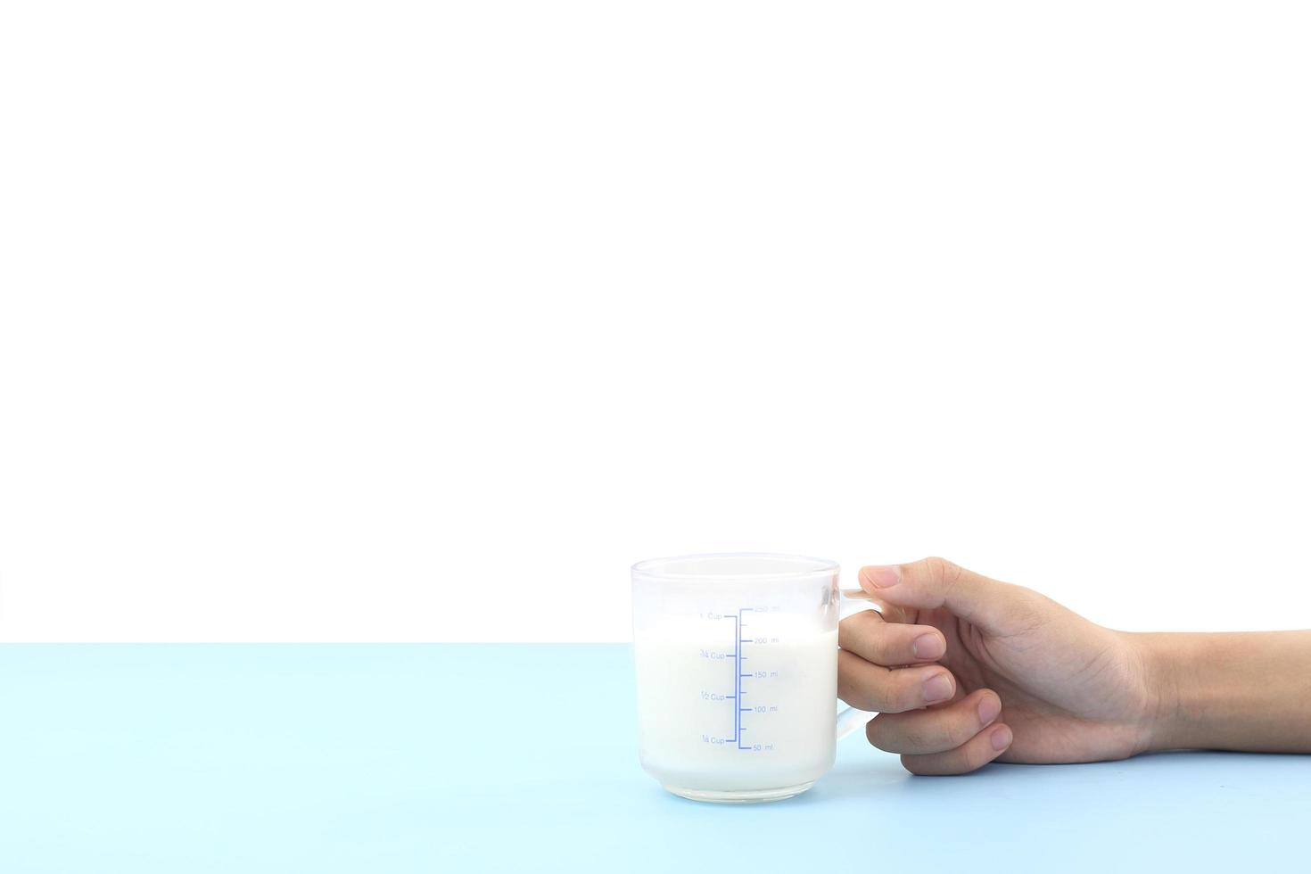 World milk day concept - Hand hold glass of fresh cold rustic cow milk - high protein and calcium on blue table against white background for breakfast in the morning. photo