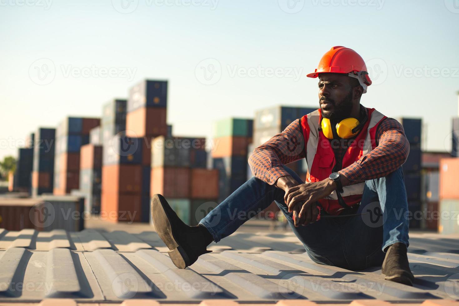 técnico o ingeniero afroamericano. siéntese cerca de un contenedor y luzca cansado y somnoliento o desempleado. concepto de transportador de carga industrial de logística. foto