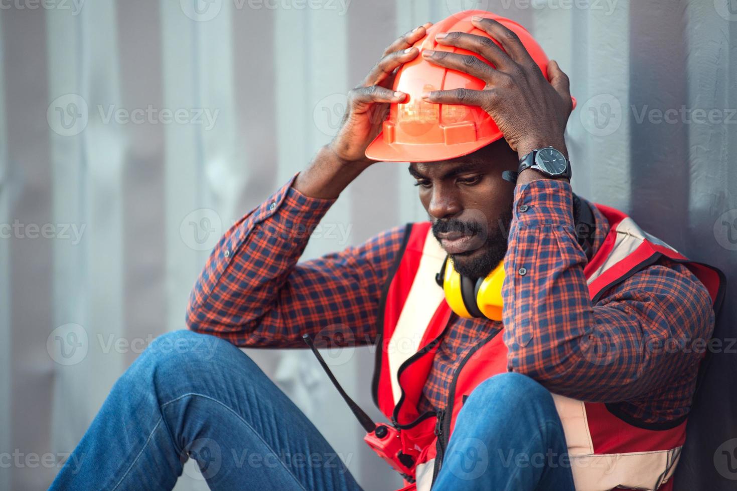 African American male technician or engineer. Sit near a container and look tired and sleepy or unemployed. Logistics industrial cargo mover concept. photo