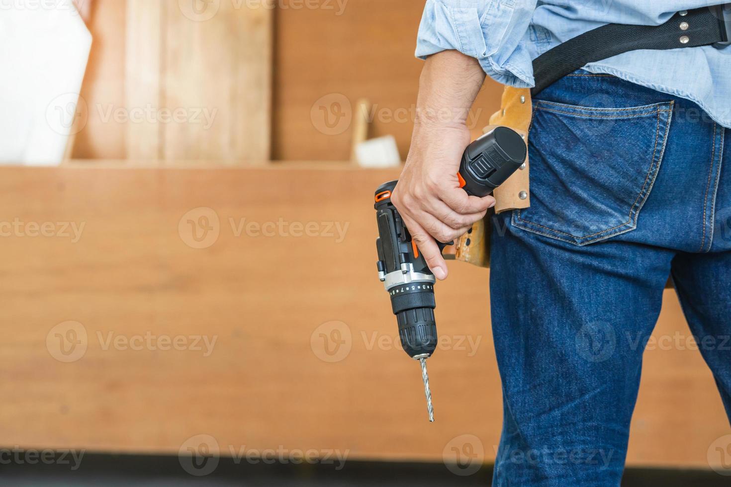 Man works in carpentry workshop. Handyman manual worker in tools belt and holding drill in his hands photo