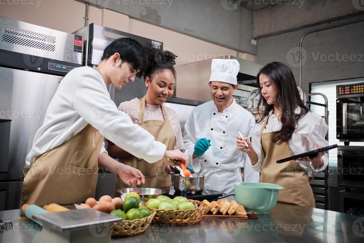 curso de cocina de hobby, chef masculino senior en uniforme de cocinero enseña a los jóvenes estudiantes de cocina a preparar, mezclar y revolver ingredientes para pasteles, pasteles de frutas en la cocina de acero inoxidable del restaurante. foto