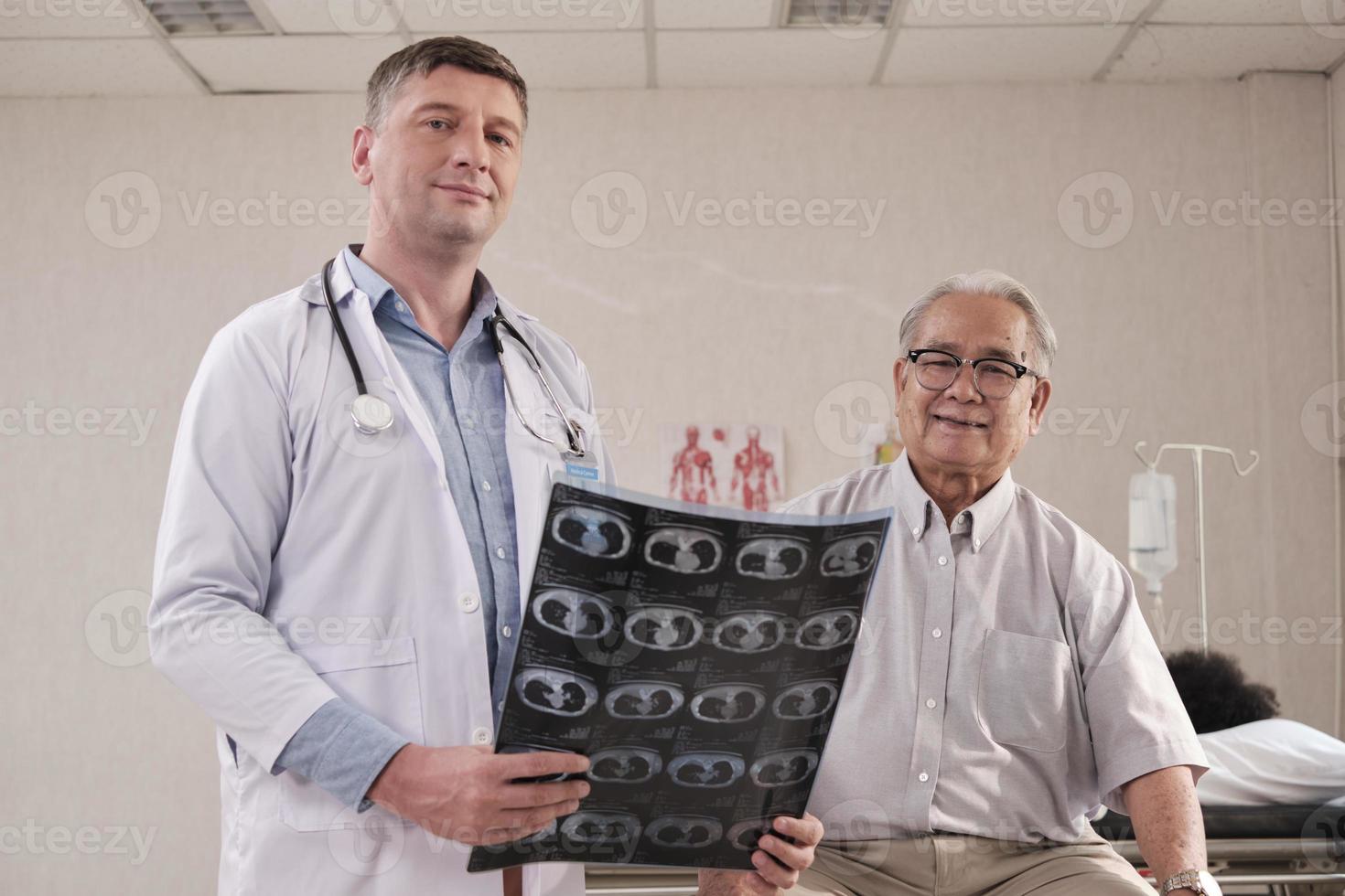 retrato de un médico caucásico en uniforme y feliz paciente senior con una sonrisa de película de rayos X y mirando la cámara en la cama de la sala de emergencias en el hospital, clínica médica para ancianos, consultor de exámenes. foto