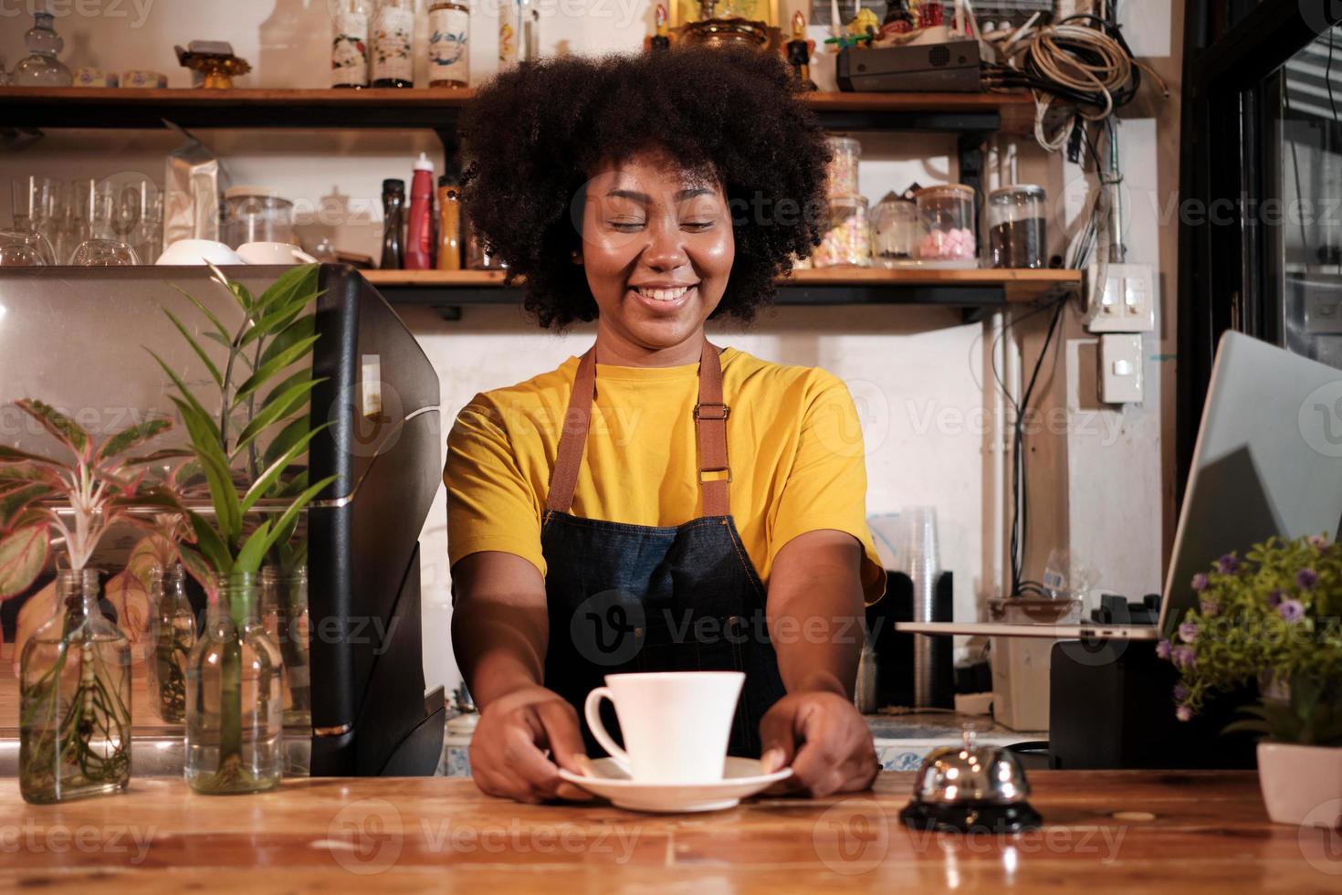 African American female barista offers cup of coffee to customer with cheerful smile, happy service works in casual restaurant cafe, young small business startup entrepreneur. photo