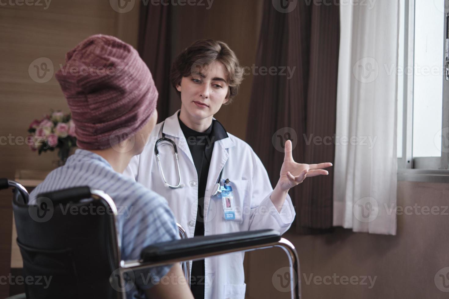 Uniformed young Caucasian female therapy doctor encouraging wheelchair male patient at window to support and motivate recovery, cancer illness after chemo medical treatment in hospital inpatient room. photo