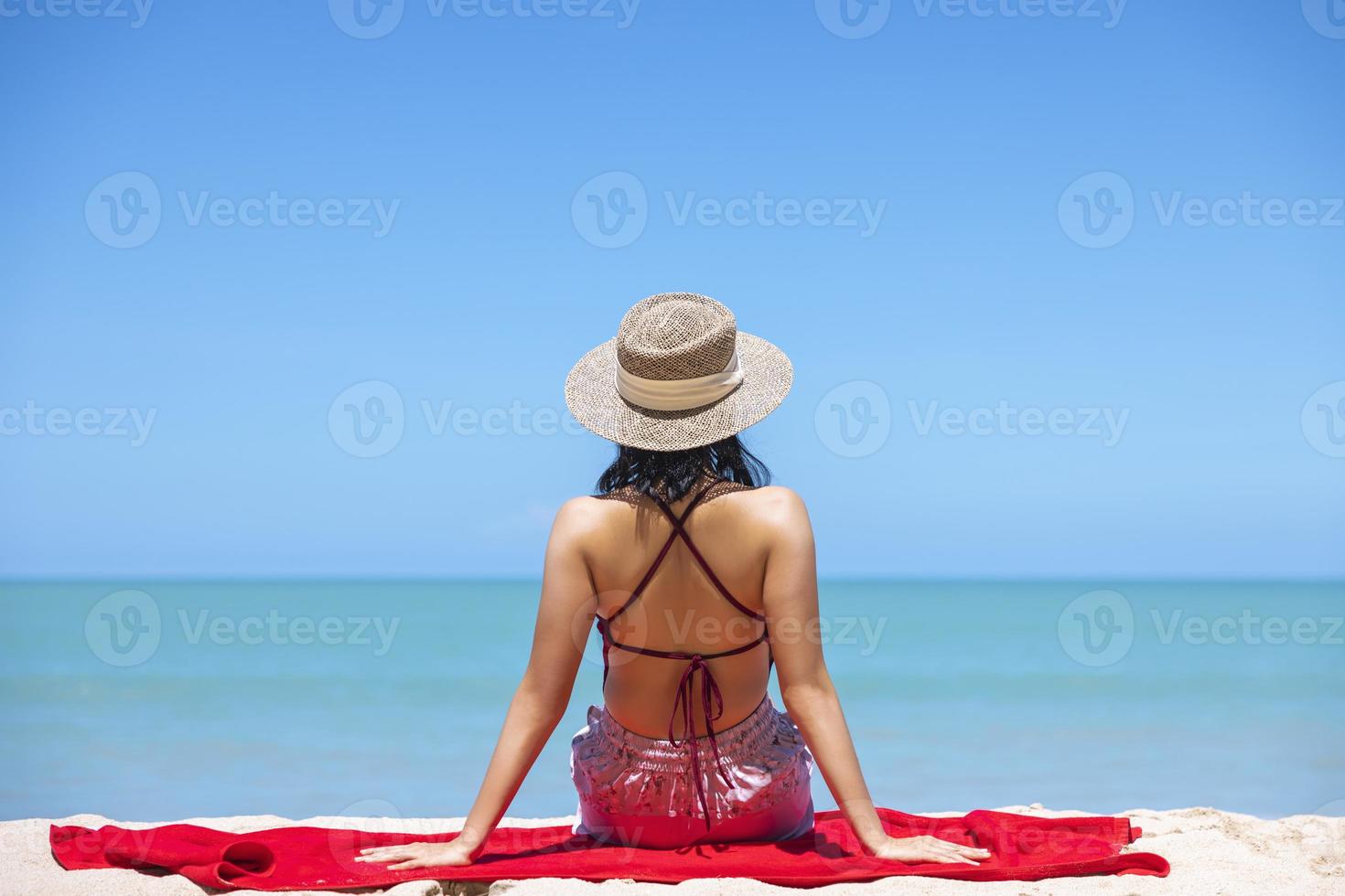 las mujeres jóvenes en bikini y sombrero de paja se sientan en la playa  tropical disfrutando