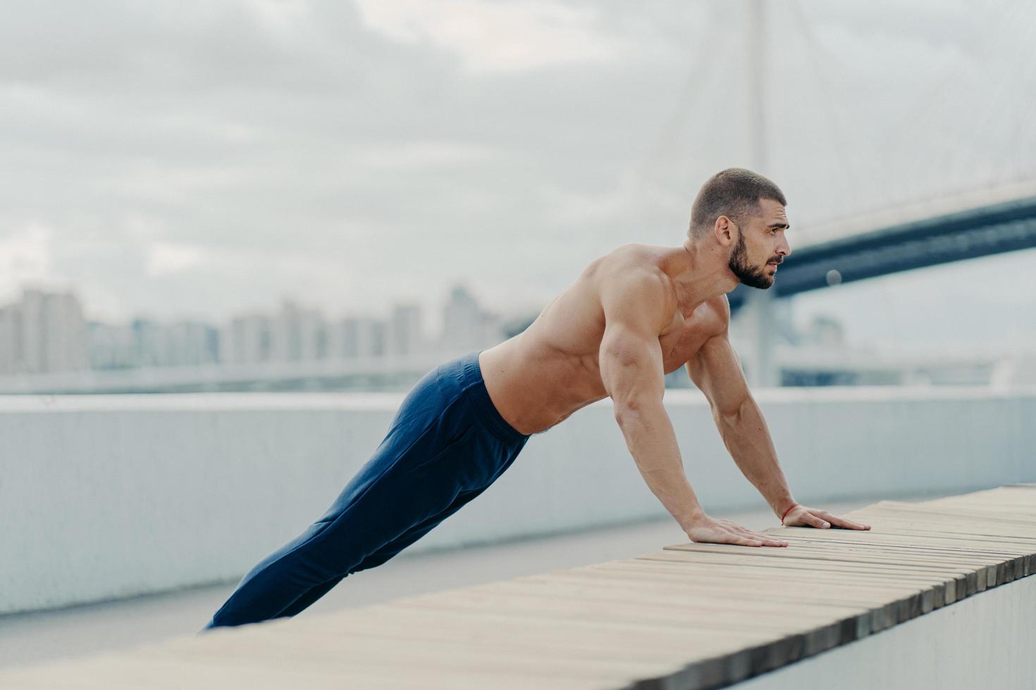 el atleta se para en la pose de la tabla hace ejercicio de empuje al aire libre respira aire fresco tiene un cuerpo fuerte y el torso desnudo motivación para mantenerse en forma y saludable lleva un estilo de vida activo. concepto de entrenamiento deportivo foto