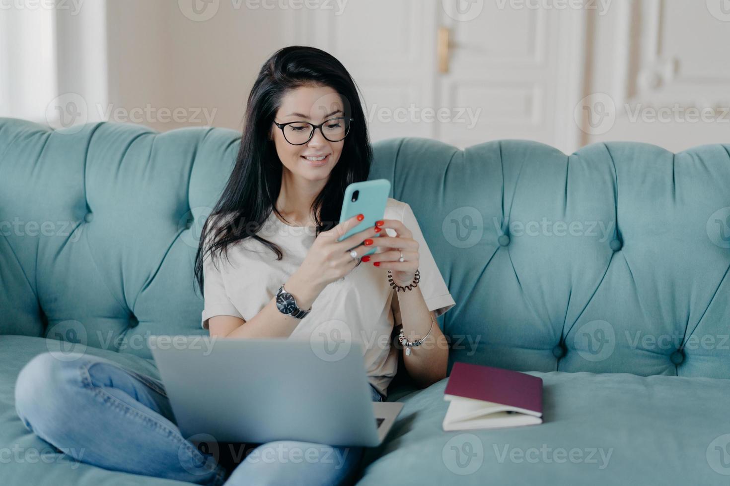 Happy female blogger chats with friends in social netwoks, works on laptop computer, poses in coworking space, sits on sofa in lotus pose, connected to wireless internet. Technology, freelancing photo