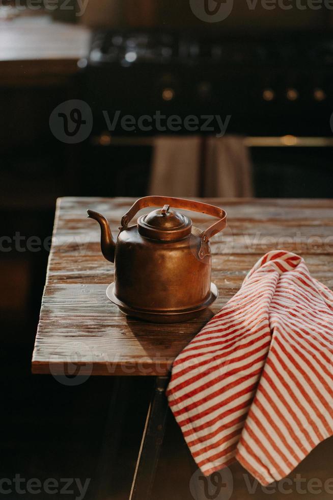 Retro aluminium kettle on wooden table with red striped towel near. Copper old teapot uses for making tea. Old fashioned kitchenware photo