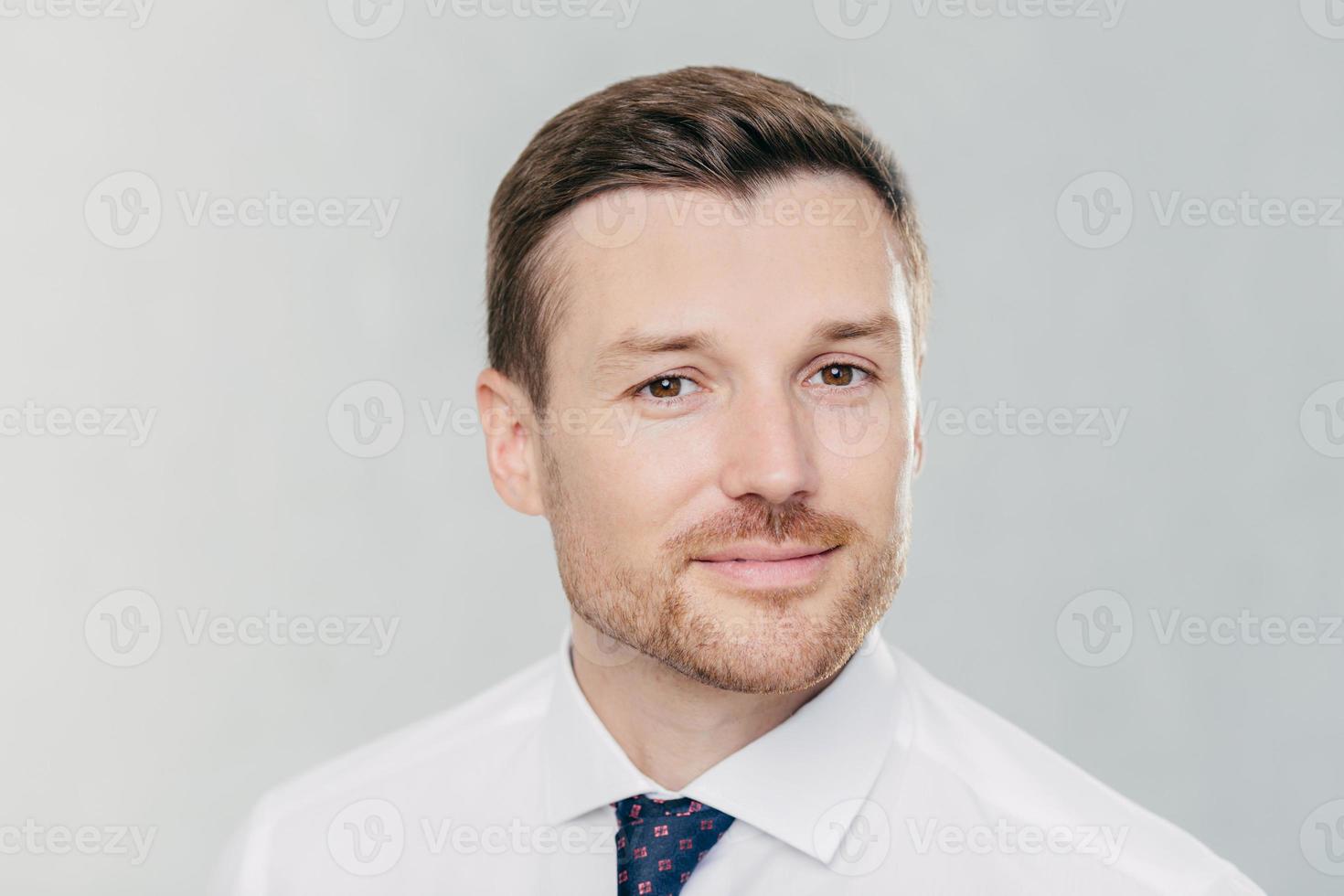 Portrait of confident unshaven businessman looks with self assured expression, ready to sign contract, poses in office against white background, wears white shirt and elegant tie. Business and people photo