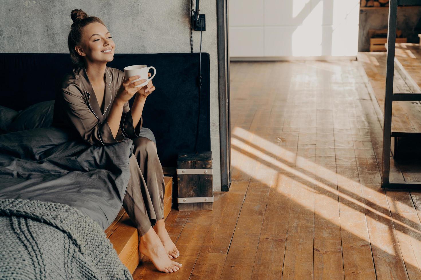 linda chica guapa con una taza de café matutino relajándose mientras se sienta en la cama foto